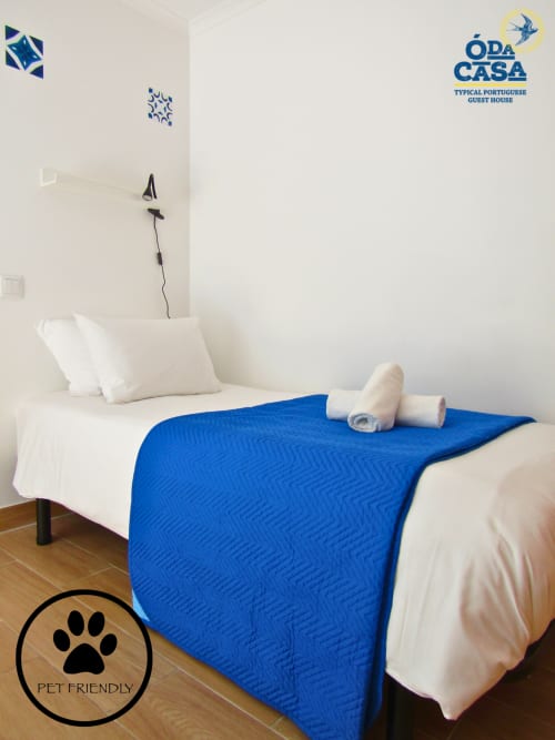 Quarto pet-friendly na casa de hóspedes Ó da Casa em Peniche com cobertor azul, almofadas brancas e toalhas enroladas