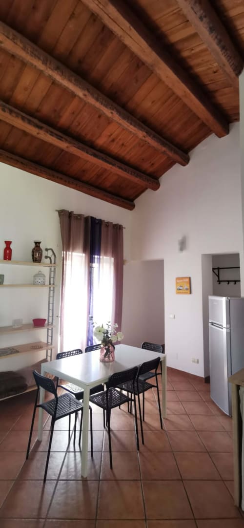 Modern dining area in Casa Bellini apartment with exposed wooden beams, white table, black chairs, and kitchen in Palermo