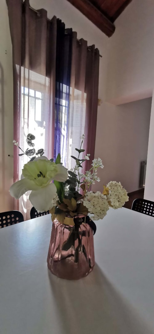 Fresh flower arrangement in pink vase on dining table at Casa Bellini apartment in Palermo with city view windows