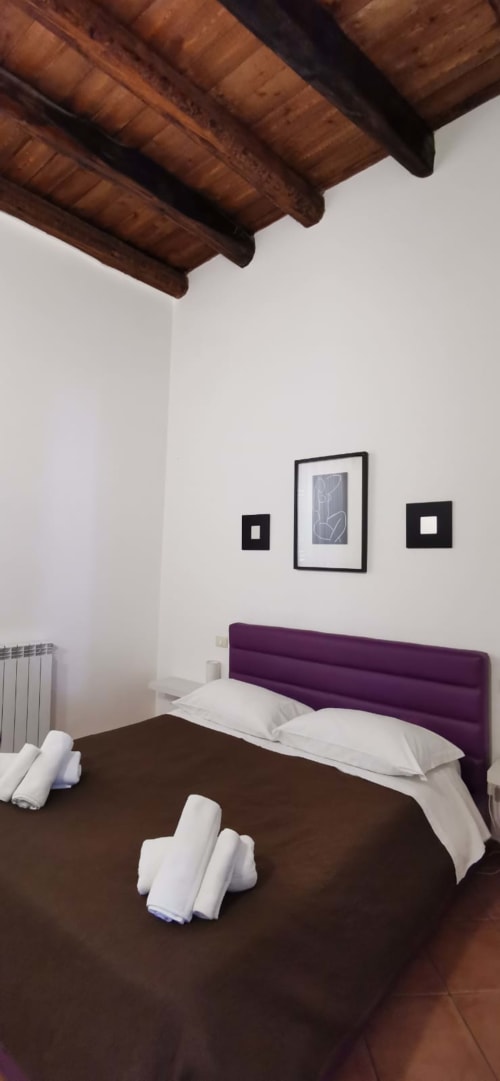 Modern bedroom at Casa Bellini Palermo with purple headboard, white pillows, exposed wooden beams, and framed artwork on
