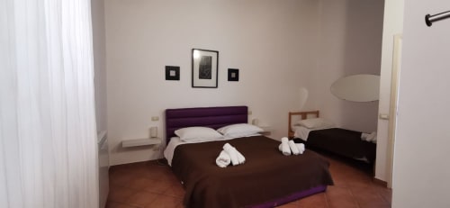 Bright bedroom in Casa Bellini apartment, Palermo, with double bed, white linens, purple headboard, terracotta floor, and