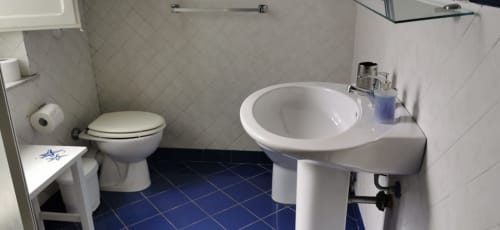 Bathroom at Casa Bellini apartment in Palermo with pedestal sink, toilet, and blue tile flooring