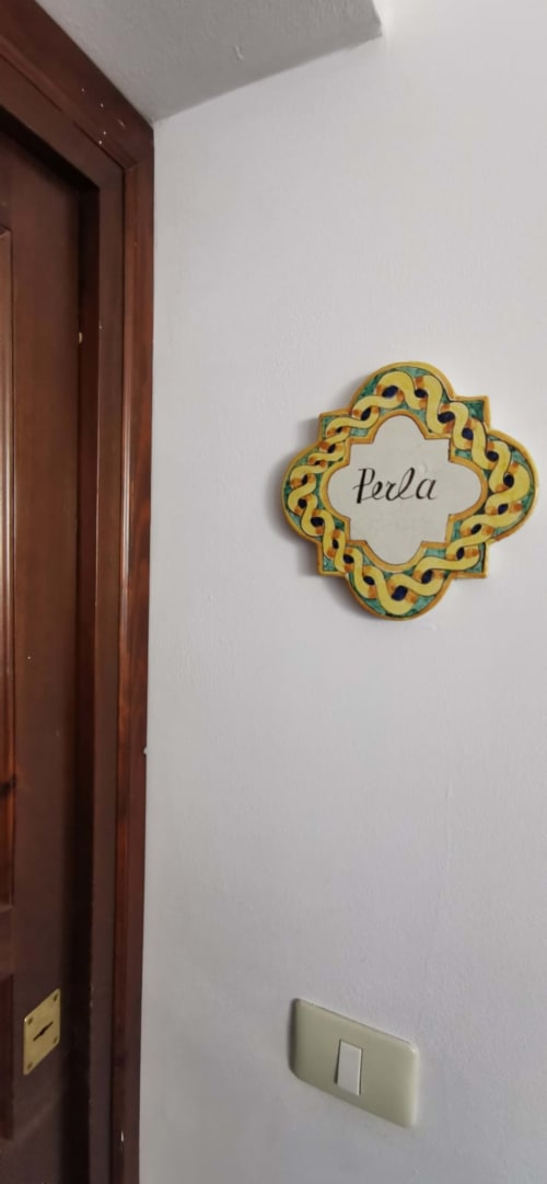 Decorative door sign reading 'Perla' on white wall next to dark wood door in Casa Bellini apartment, Palermo