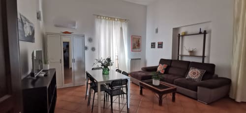 Perla Apartment living room at Casa Bellini, Palermo featuring dark sofa, dining table, TV, and city views