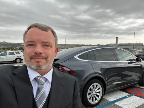Immobilienmanager von La Conciergerie De Franck, Boissieres, steht auf einem Parkplatz neben einer schwarzen Limousine