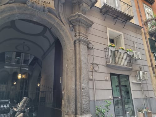 Naples historic building facade with arched entrance, balcony with flowers, and green shutters at B&B Il Conservatorio