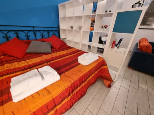 Modern bedroom at B&B Il Conservatorio Naples with red and orange striped bedding, white shelving unit, blue walls, and