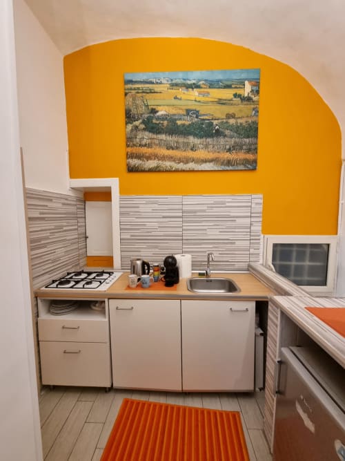 Compact kitchenette with bright yellow accent wall, gas stove, sink, and countryside artwork in Majorana apartment at B&B Il
