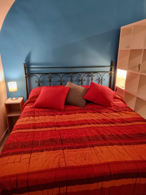 Modern bedroom in Naples B&B with red bedding, ornate headboard, blue walls, wooden shelving, and warm lighting