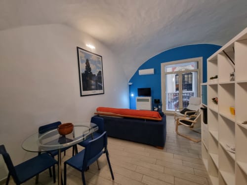 Modern apartment living area in Naples with blue accent wall, dining table, dark sofa, and balcony access at B&B Il