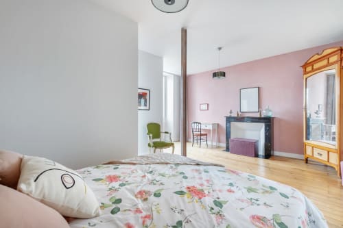 Chambre spacieuse à La Maison D'olivier B&B avec literie fleurie, murs roses, parquet et vue sur un monument