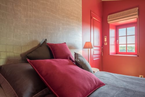 Chambre moderne à la Conciergerie Des Climats à Beaune avec coussins bordeaux, mur de brique, porte rouge et fenêtre sur la montagne