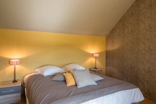 Chambre moderne à la Conciergerie Des Climats, Beaune avec murs jaunes, mur d'accent texturé, lit avec oreillers et ambiance chaleureuse