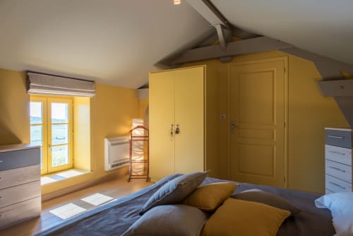 Chambre jaune éclatante à la Conciergerie Des Climats à Beaune avec literie bleue, grande armoire et vue sur jardin