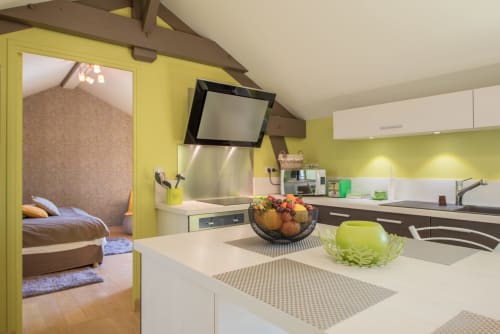Cuisine jaune moderne avec plans de travail blancs, appareils en inox et accès à la chambre dans un appartement de Beaune