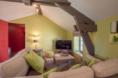Appartement moderne sous les toits à la Conciergerie Des Climats, Beaune avec murs jaunes, canapés beige, touches vertes, TV et poutres apparentes