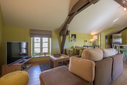 Lumineux appartement Beaune jaune vif avec canapé beige, télévision, coin repas et poutres apparentes