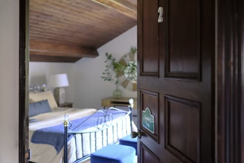 Dark wooden door open to bedroom at Villa Várzea guesthouse in Várzea, Portugal, with metal bed frame visible