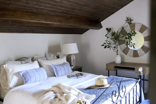 Elegant bedroom at Villa Várzea with blue striped pillows, metal bed frame, wooden beams, and decorative round mirror