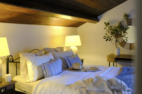 Cozy bedroom at Villa Várzea B&B in Várzea with striped blue pillows, warm lighting, and wooden ceiling beams