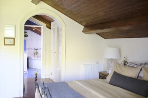 Bedroom at Villa Várzea with arched doorway to bathroom, wooden beams, and bed with neutral pillows