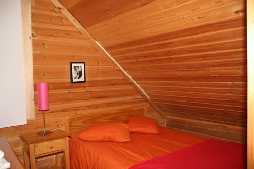 Aconchego do quarto do chalé em Cota 1500 com roupa de cama laranja, teto inclinado, luminária rosa e vistas da serra em Penhas da Saúde