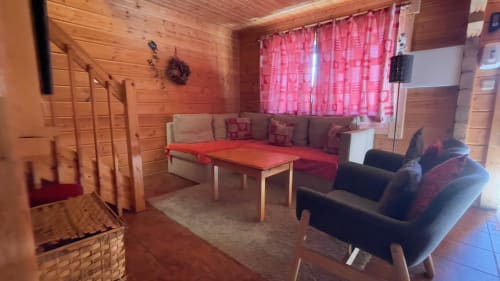 Aconchegante sala de estar na villa Cota 1500 com paredes em madeira, assentos coloridos e cortinas rosa com vista para as montanhas