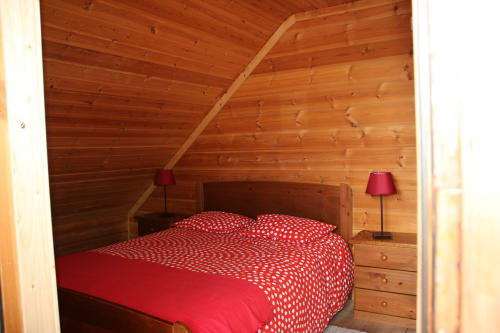 Quarto aconchegante com painéis de madeira no chalé Cota 1500, cama com roupa de cama vermelha com bolinhas e vistas para a montanha em Penhas da Saúde