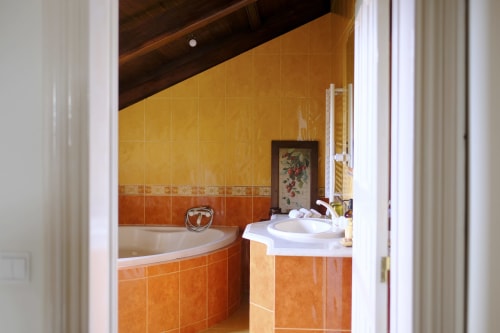 Bathroom at Villa Várzea B&B with orange tiled walls, corner bathtub, and vanity sink in Várzea, Portugal
