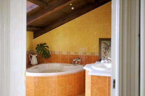 Luxurious bathroom at Villa Várzea with curved corner bathtub, yellow and orange tile work, wooden ceiling beams, and