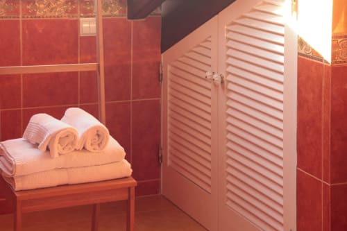 Luxurious bathroom at Villa Várzea B&B with red tile walls, white louvered doors, and rolled towels on wooden shelf