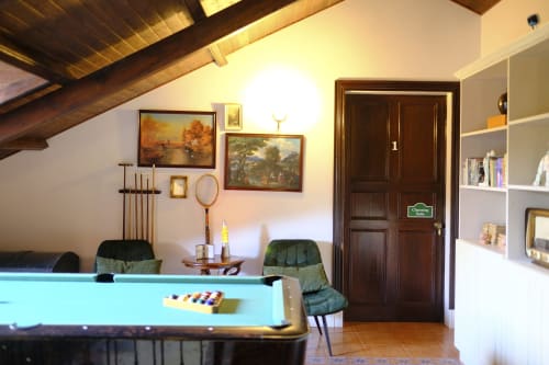 Cozy game room at Villa Várzea B&B in Várzea with billiards table, vintage artwork, dark wood door, and shelving.