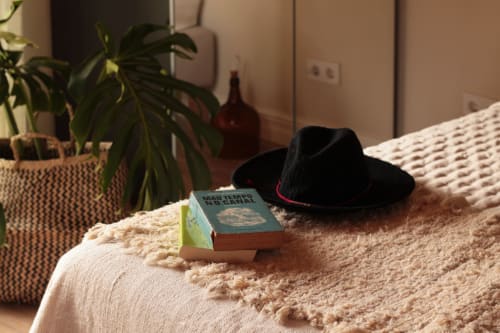 Black cowboy hat and book on cream textured bed at Villa Várzea guesthouse in Várzea, Portugal