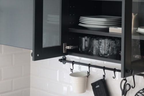 Modern kitchen cabinet at Villa Várzea B&B with white subway tiles, stacked plates, glasses, and black hooks holding utensils