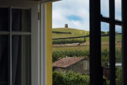 View from Villa Várzea window of green fields, traditional stone structure, and hillside in Várzea, Portugal