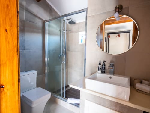 Modern bathroom at Villa Várzea with glass shower, circular mirror, white sink, and wooden door in Várzea, Portugal