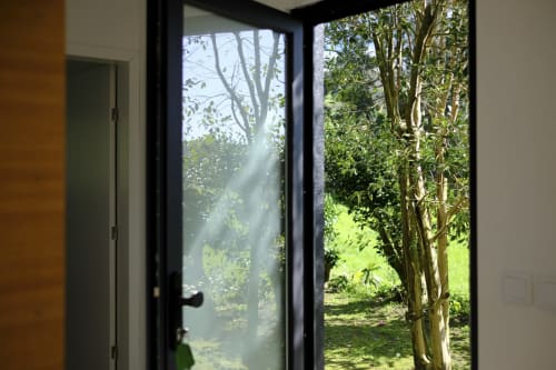 Black-framed glass doors at Villa Várzea opening to sunlit garden with trees and lush green landscape in Várzea, Portugal