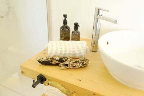 Wooden bathroom vanity at Villa Várzea with white vessel sink, toiletries, towel, and decorative stones