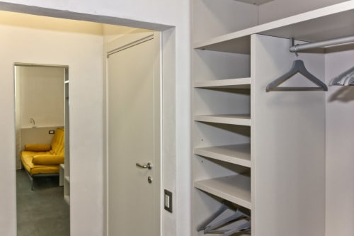 Guardaroba della Camera 3 di Casa Mirko con ripiani, appendiabiti e vista sulla camera da letto con sedia gialla