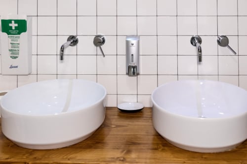 Two white ceramic vessel sinks at Casa Mirko B&B in Arezzo with wall-mounted faucets and Lucant toiletries dispenser
