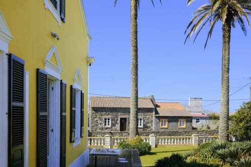 Bright yellow villa with blue shutters at Villa Várzea guesthouse in Portugal, featuring palm trees and stone buildings