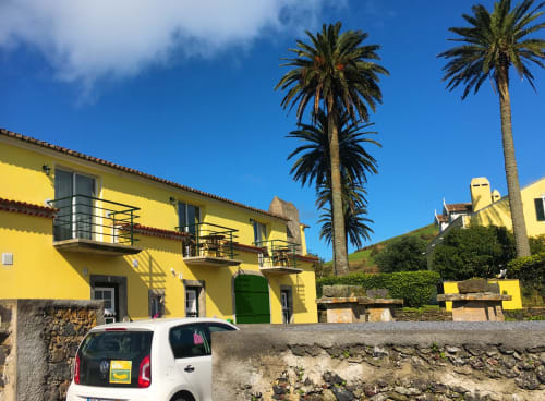 Bright yellow Villa Várzea guesthouse in Várzea, Portugal with palm trees, balconies, and stone courtyard