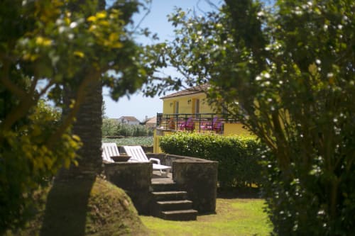 Garden view of yellow house at Villa Várzea B&B in Várzea, Portugal with lounge chairs and green hedges