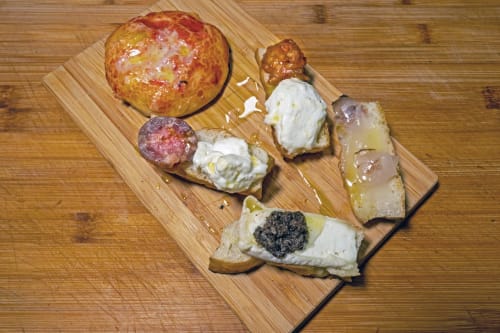 Gourmet appetizers on wooden board at Casa Mirko B&B in Arezzo, featuring cured meats, cheese, and crostini
