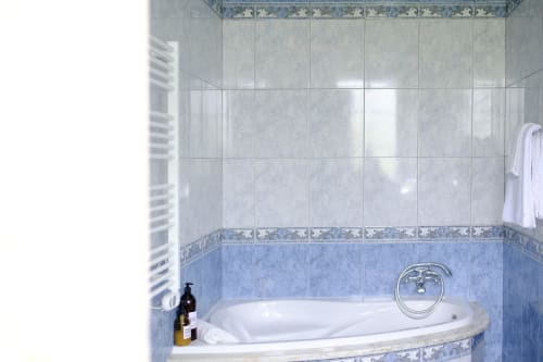 Elegant bathtub in Garden Suite at Villa Várzea with blue and gray tile, chrome fixtures, and white towels