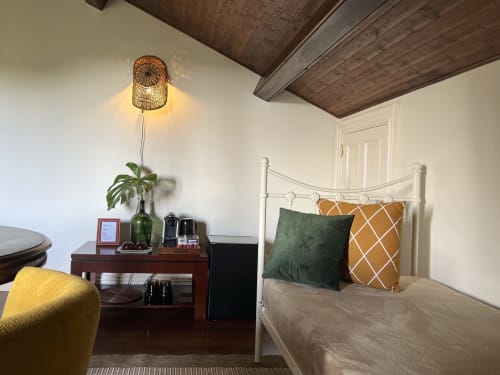 Charming Suite at Villa Várzea with white metal bed, green and gold pillows, wooden ceiling, and wicker lamp