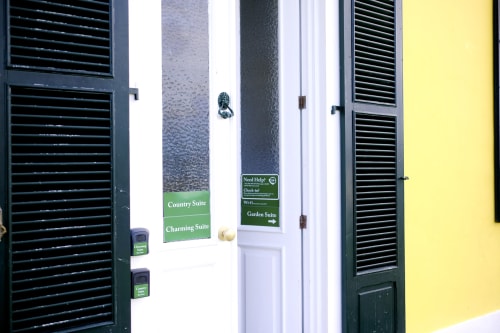 Villa Várzea entrance with green suite signs for Charming and Garden suites, dark shutters, white walls, yellow accent wall