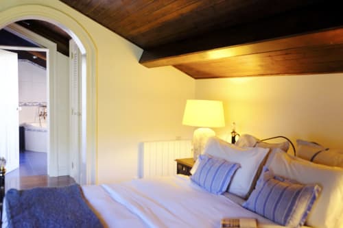 Country Suite bedroom at Villa Várzea with blue striped pillows, warm lighting, wooden beams, and ensuite bathroom entrance