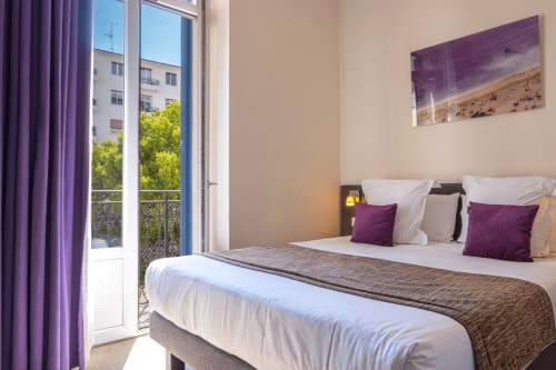 Modern hotel bedroom at Hôtel De La Fontaine in Nice with purple accents, balcony view, and beach artwork