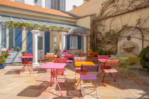 Patio vivace dell'Hôtel De La Fontaine a Nizza con sedie e tavoli colorati, atmosfera di giardino mediterraneo